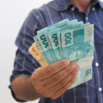 Mão segurando notas de 100 reais em português do Brasil